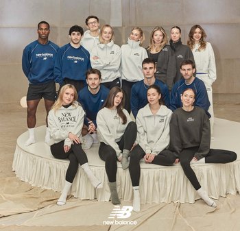 Grupo de hombres y mujeres vestidos con ropa deportiva de New Balance, posando sobre y alrededor de una plataforma circular en un entorno interior de tonos neutros.