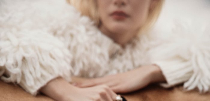 Personne portant un pull blanc texturé tenant un sac à main en daim marron posé sur la fourrure beige d'un animal.