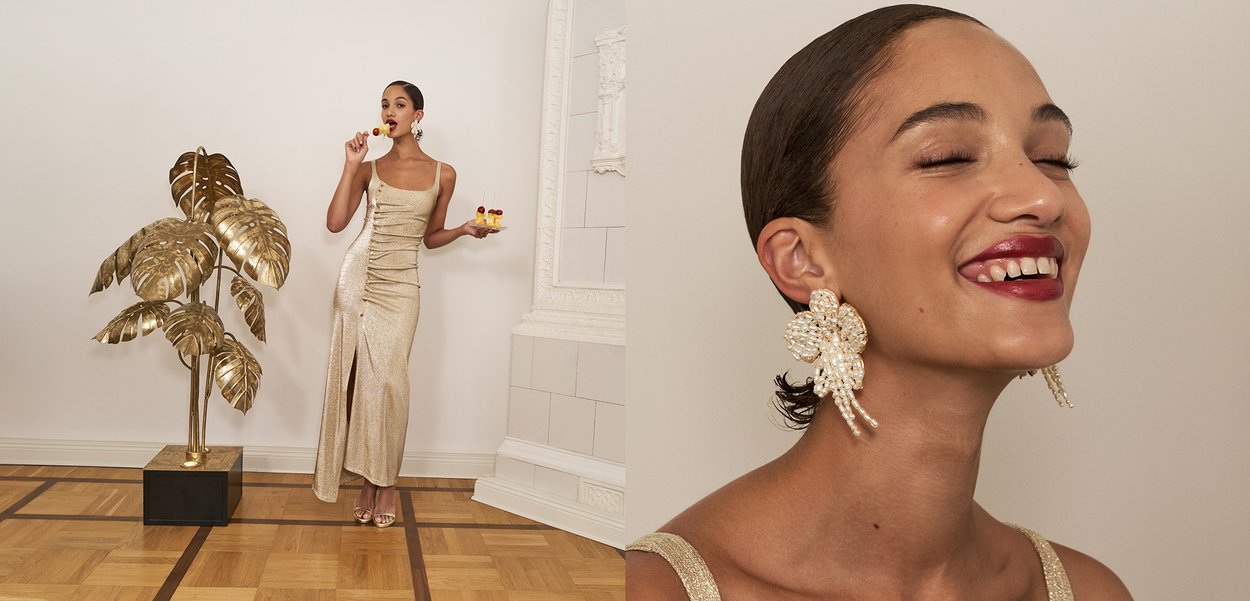 Zlatna haljina sa šljokicama koja ima visoki prorez i nabranu teksturu; model drži desert i nosi velike cvjetne naušnice; zlatna biljka u blizini.
