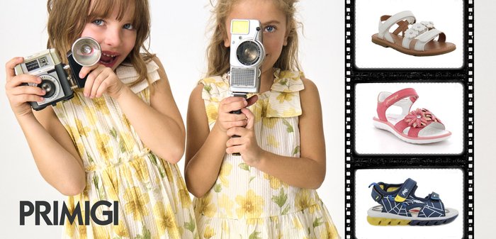Young girl in yellow floral dress holding vintage camera beside three children’s sandals: white, pink flowered, and blue with yellow soles.