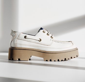 Witte leren veterschoen met dikke bruine geribbelde zool, moc-toenaad en metalen oogjes, zijaanzicht met schaduw.