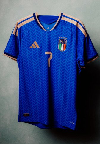 Niebieska koszulka piłkarska Włoch z złotym logo Adidas, numer 7 oraz herb z włoską flagą i czterema gwiazdkami na szarym tle.