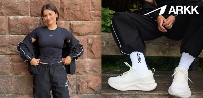 Person, der sidder på en træbænk iført hvide ARKK-sneakers, hvide ARKK-sokker og sorte bukser med reflekterende striber.