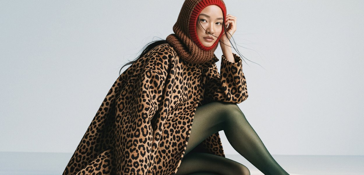 Oversized kappa med leopardmönster i bruna nyanser, stickad röd- och brun huvudscarf, gröna strumpbyxor, slät textur, lös passform och långa ärmar.