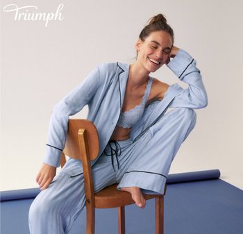 Set di pigiami azzurro chiaro con dettagli neri, composto da una camicia con bottoni e pantaloni larghi, abbinato a un bralette in pizzo. Sfondo con una sedia di legno.