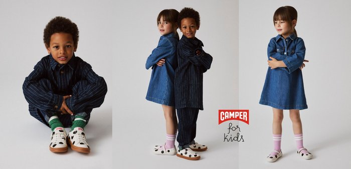 Jong kind zittend in kleermakerszit, gekleed in een donker pak met krijtstreep, groene sokken en witte schoenen met zwarte vlekken en bruine zolen.