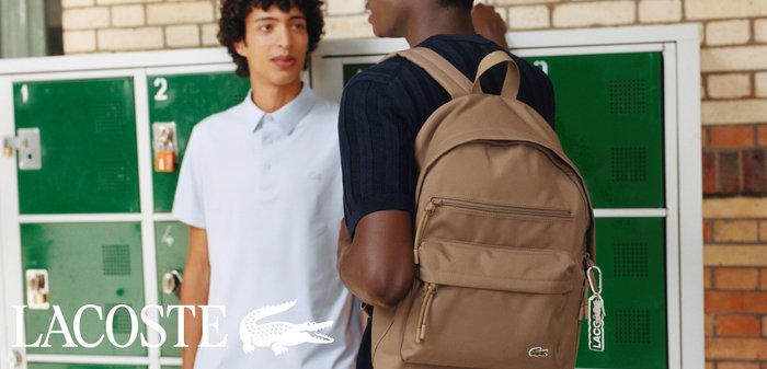 Due studenti parlano vicino a degli armadietti verdi, uno indossa una polo bianca, l'altro ha uno zaino beige e un portachiavi Lacoste.