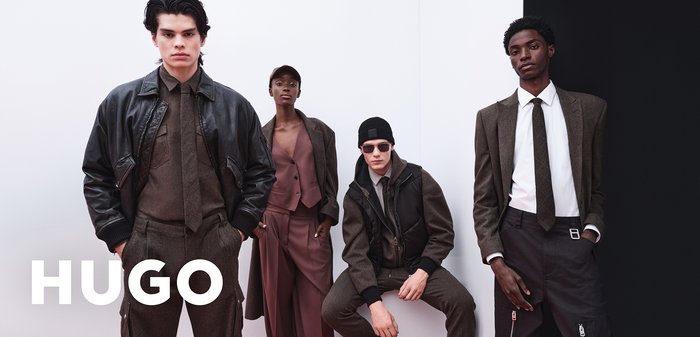 Gruppe von vier Models in moderner Kleidung: eine dunkle Lederjacke, braune Anzüge, eine Weste und verschiedene Accessoires vor einem minimalen Hintergrund.