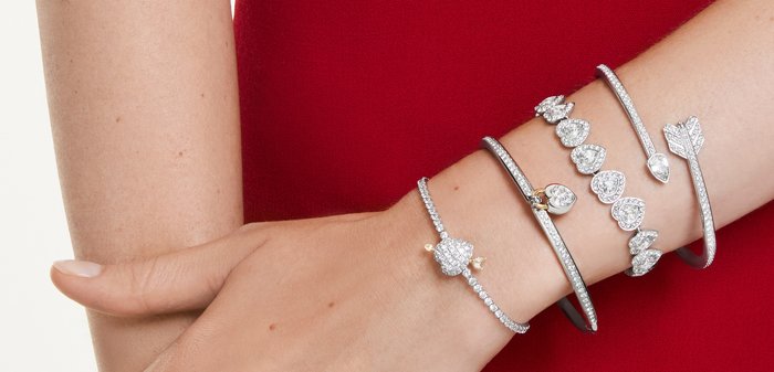 Rechter onderarm en hand met vijf zilveren ringen bezet met diamanten en vier zilveren armbanden met hart- en pijldesigns, tegen een rode mouw.