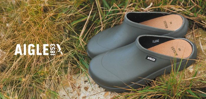 Sabots en caoutchouc vert foncé avec une finition lisse, arborant un logo AIGLE noir et une semelle intérieure en liège. Design à bout rond et à petit talon.