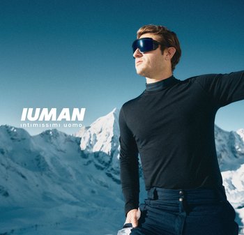 Schwarzes Langarmshirt, elegantes Design, getragen mit dunklen Hosen. Sonnenbrille mit großen, kantigen Linsen, verschneite Berge im Hintergrund.