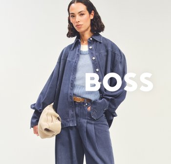 Vrouw die een losse, donker denim jack en broek draagt met een lichtblauwe trui, houdt een beige tas vast, met de tekst "BOSS" naast haar op een effen achtergrond.