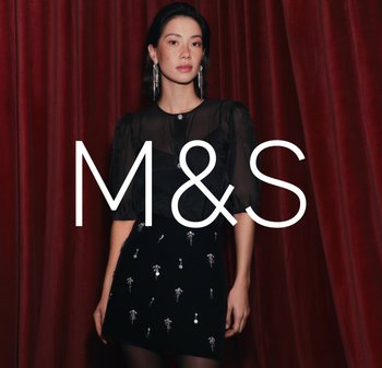 Black mini skirt with metallic floral embellishments, sheer puff-sleeve top, model posing against a red velvet background. M&S branding prominent.