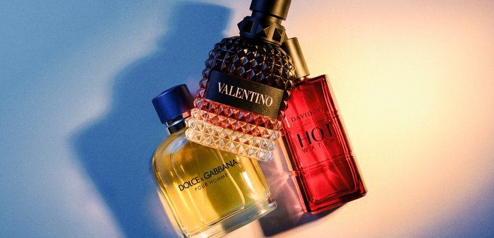 Trois flacons de parfum étiquetés Dolce & Gabbana, Valentino et Davidoff Hot Water avec lumière et ombre sur une surface plane.