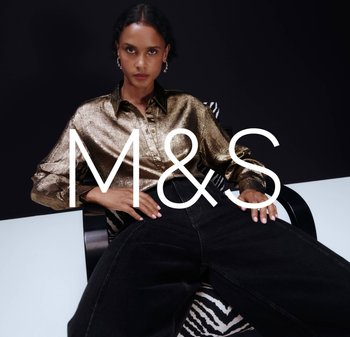 Woman with serious expression wearing metallic gold shirt and black pants seated on zebra-patterned chair against dark background.