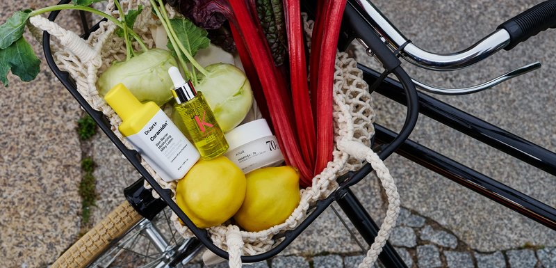 Panier avec des produits de soins de la peau et des produits frais. Comprend des bouteilles jaunes, un pot blanc, du kohlrabi vert et des rhubarbes rouges vibrantes, sur un vélo.