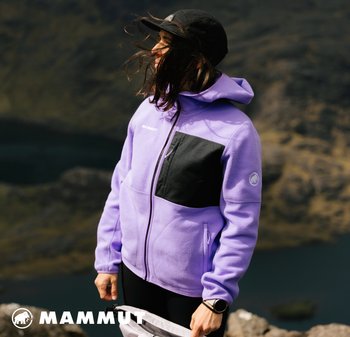 Lila Fleecejacke mit einer schwarzen Patchtasche und Logo. Verfügt über eine Kapuze und einen Reißverschluss, vor einer natürlichen Außenkulisse.