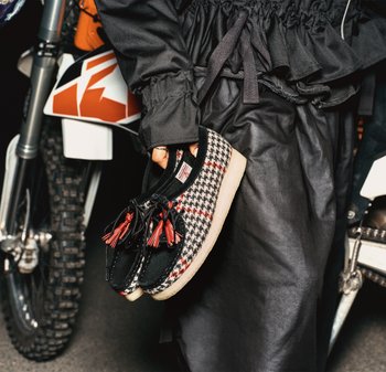 Chaussures noires et rouges à motif carreaux, ornées de franges et d'un design pied-de-poule. La semelle est de couleur claire, avec un bout arrondi et une texture lisse.