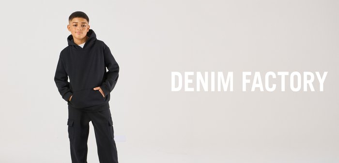 Boy wearing a black hoodie and cargo trousers stands with his hands in his pockets beside the text "DENIM FACTORY" on a plain light background.