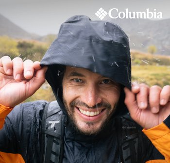 Veste noire imperméable à capuche avec une texture visible, portée par un homme souriant, agrémentée de détails orange, des gouttes de pluie tombant autour de lui.