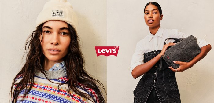 Crème gebreide beanie met logo-patch; kleurrijke, patroontrui met rode en blauwe strepen; lichtblauwe overhemd met kraag eronder. Haar losjes gestyled.