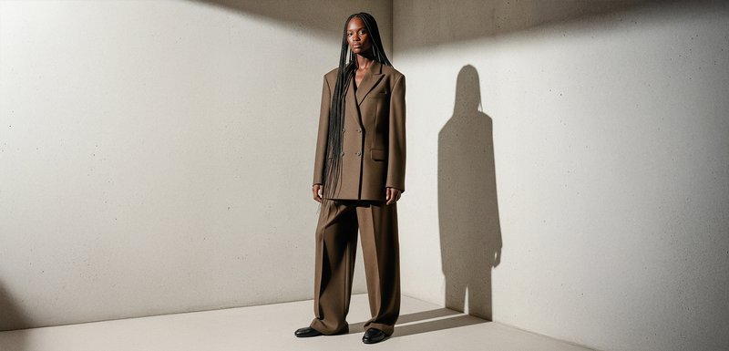 Costume marron sur mesure en tissu lisse, comprenant une veste croisée avec deux poches avant et un pantalon à jambes larges.