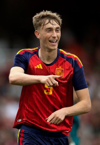 Νέος male ποδοσφαιριστής σε κόκκινη και μπλε φανέλα Ισπανίας, χαμογελά και δείχνει μπροστά κατά τη διάρκεια ενός αγώνα.