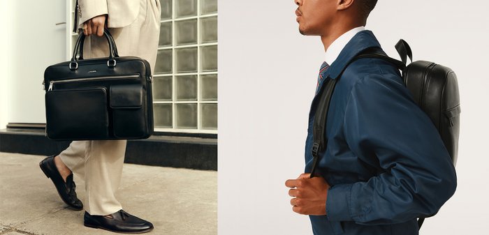 Man in blauwe jas en gestreepte stropdas draagt een zwarte leren rugzak op zijn rug, van opzij getoond tegen een effen achtergrond.