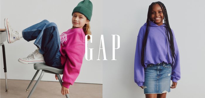 To børn: den ene iført en pink sweatshirt og denim jeans, den anden i en lilla hættejakke og denimnederdel. Begge sidder opad en neutral baggrund.