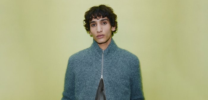 Grau Wolljacke mit hohem Kragen und Reißverschluss vorne, mit einer weichen Textur. Das Modell steht vor einem blassgrünen Hintergrund.