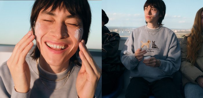 Une personne aux cheveux mi-longs foncés portant un sweat-shirt gris applique de la crème sur son visage, affichant une expression détendue et une texture de peau naturelle.