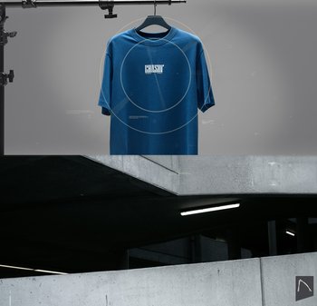 Blauw T-shirt met korte mouwen met een wit logo in het midden van de voorkant. De achtergrond van de display toont een betonnen structuur en gedimde verlichting.