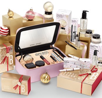 Rosa sminkväska med spegel och olika kosmetika, omgiven av gyllene och mönstrade presentlådor, julprydnader och hudvårdsprodukter.