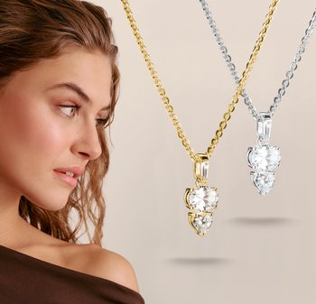 Woman with loose curly hair looks at two hanging necklaces with round and heart-shaped clear gemstone pendants, one gold and one silver.