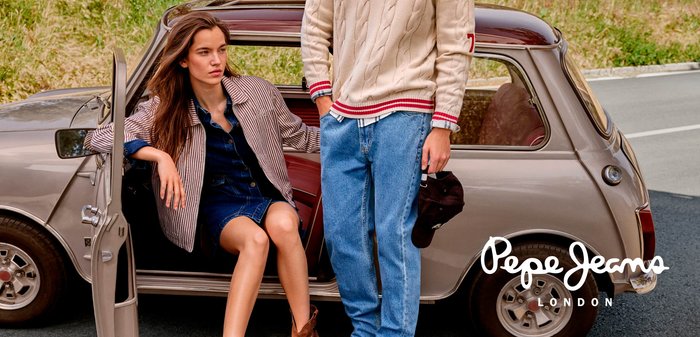 Un'auto d'epoca marrone parcheggiata con un modello in giacca a righe e vestito di denim, e una persona in un maglione di pelliccia crema e jeans blu.