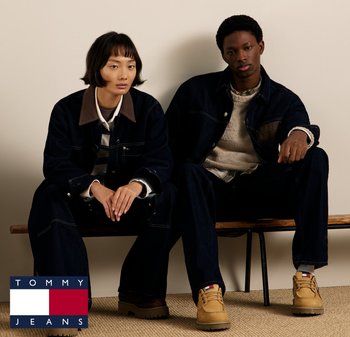 Dżinsowe kurtki i spodnie w ciemnoniebieskim kolorze z brązowymi akcentami, noszone na jasnych swetrach. Beżowe buty z detalem logo. Neutralne tło.