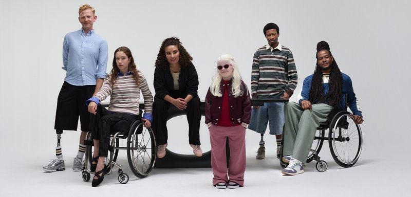 Six personnes, dont deux en fauteuils roulants, portent des tenues variées : des chemises décontractées, des pulls et des pantalons dans différentes couleurs et textures.