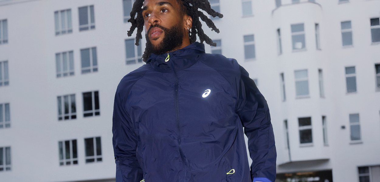 Chaqueta deportiva azul marino con cremallera frontal, logo reflectante y acentos en amarillo neón. Tejido ligero, textura suave y diseño ajustado.