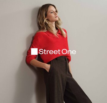 Pull rouge en laine bouclée avec un col, associé à un pantalon large et sombre. Le modèle a de longs cheveux ondulés et est appuyé contre un mur.