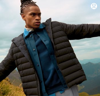 Giacca a vento nera con una finitura testurizzata, indossata sopra una maglietta teal e un maglione scuro. Bottoni visibili e un cappuccio aggiungono dettagli.