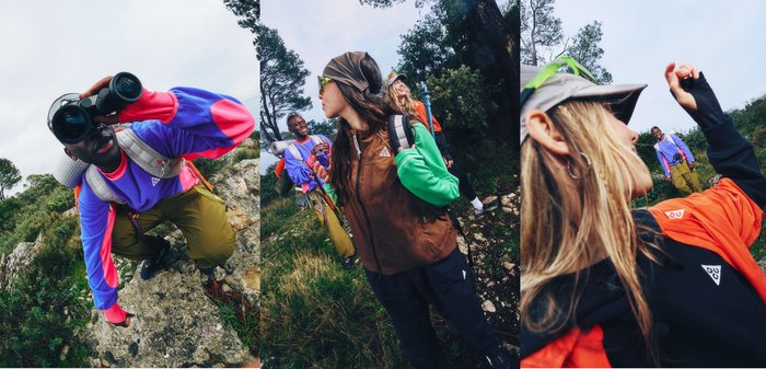 Tres senderistas diversos con ropa de exterior exploran un sendero rocoso y boscoso bajo un cielo despejado.