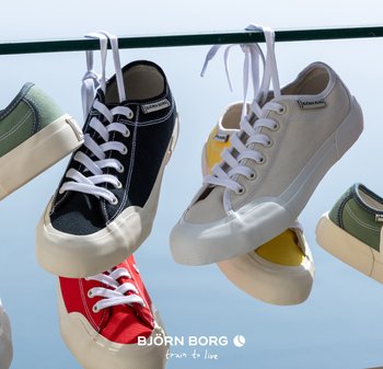 Färgglada Björn Borg-sneakers i svart, vitt, rött, gult och grönt hänger i skosnörena från en horisontell stång mot en klar himmel.
