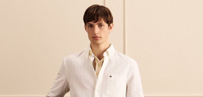 Weisses Hemd mit Knopfleiste und vertikalen Streifen, aus Baumwollstoff, Brusttasche mit einem Logo, über einem beigen, mit Kragen versehenen Hemd getragen.