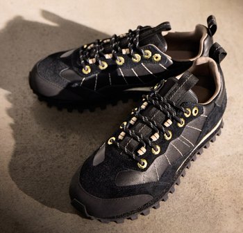Schwarze Sportschuhe mit Obermaterial aus Wildleder und Synthetik, ausgestattet mit gelben Ösen, dicken Schnürsenkeln und robusten Sohlen für gute Traktion.