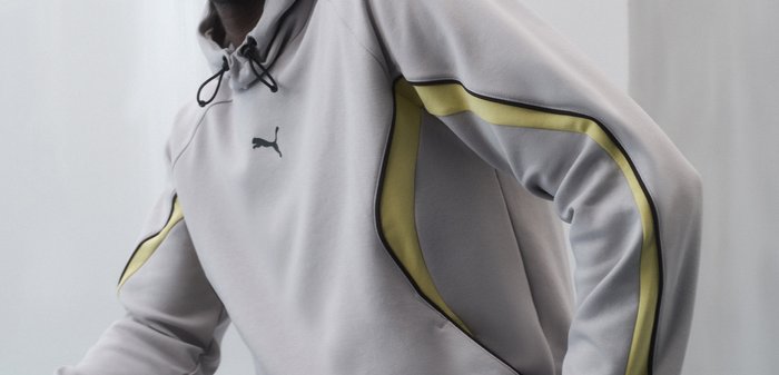 Крупен план на човек, носещ светлосиво худи Puma с черни връзки и жълти ивици на ръкавите.