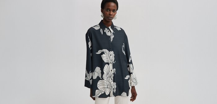 Chemise boutonnière bleu marine avec un grand imprimé floral blanc, coupe décontractée et manches longues. Fabrication en tissu lisse avec une texture douce.