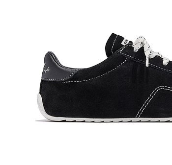 Zapatilla de perfil bajo de ante negro con costuras blancas, suela de goma blanca, cordones blancos con patrón y marca "Converse" en la lengüeta y el talón.