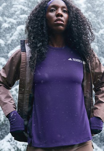 Μωβ αθλητική μπλούζα με λογότυπο, συνδυασμένη με καφέ εξωτερικό μπουφάν. Διαθέτει στρογγυλή λαιμόκοψη και μακριά μανίκια, σε ένα χιονισμένο φόντο.