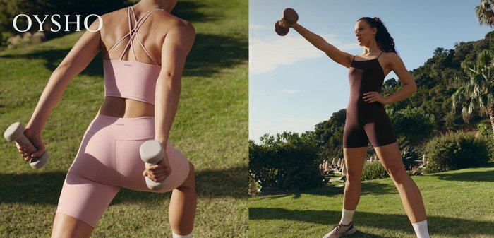 Woman in pink sportswear performing an outdoor exercise holding light dumbbells with greenery in the background.