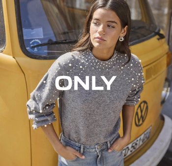 Jongeman in een grijze trui met parels en jeans, staand voor een gele vintage Volkswagen bus.